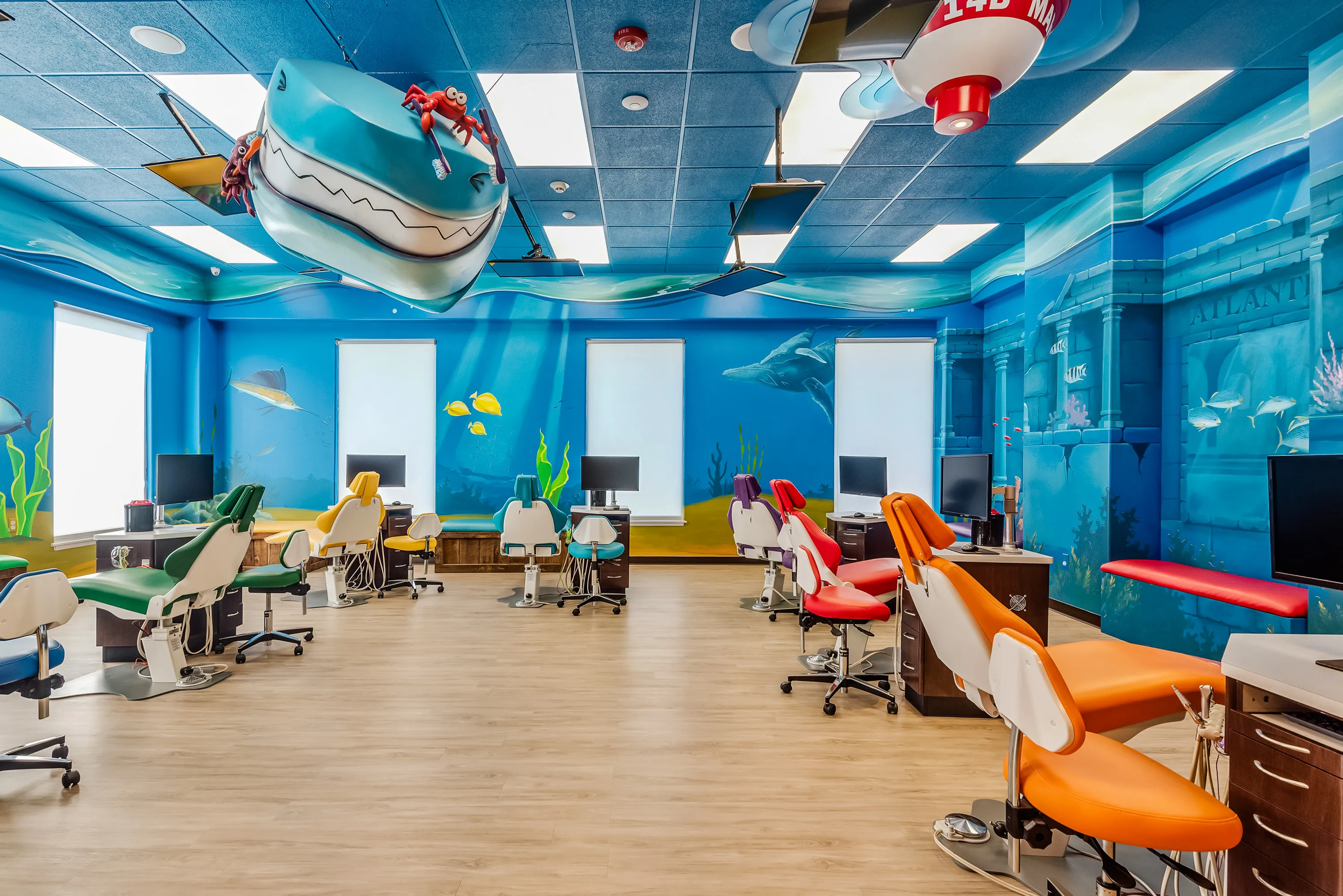 The Super Smiles open treatment bay, an underwater mural with a whale suspended from the ceiling above rows of colorful dental chairs