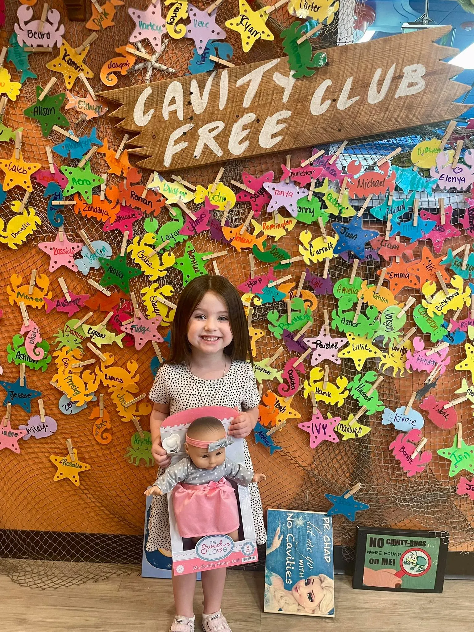 A young patient at the Cavity Free Club wall holding a prize, in front of a net covered wall of colorful named stars
