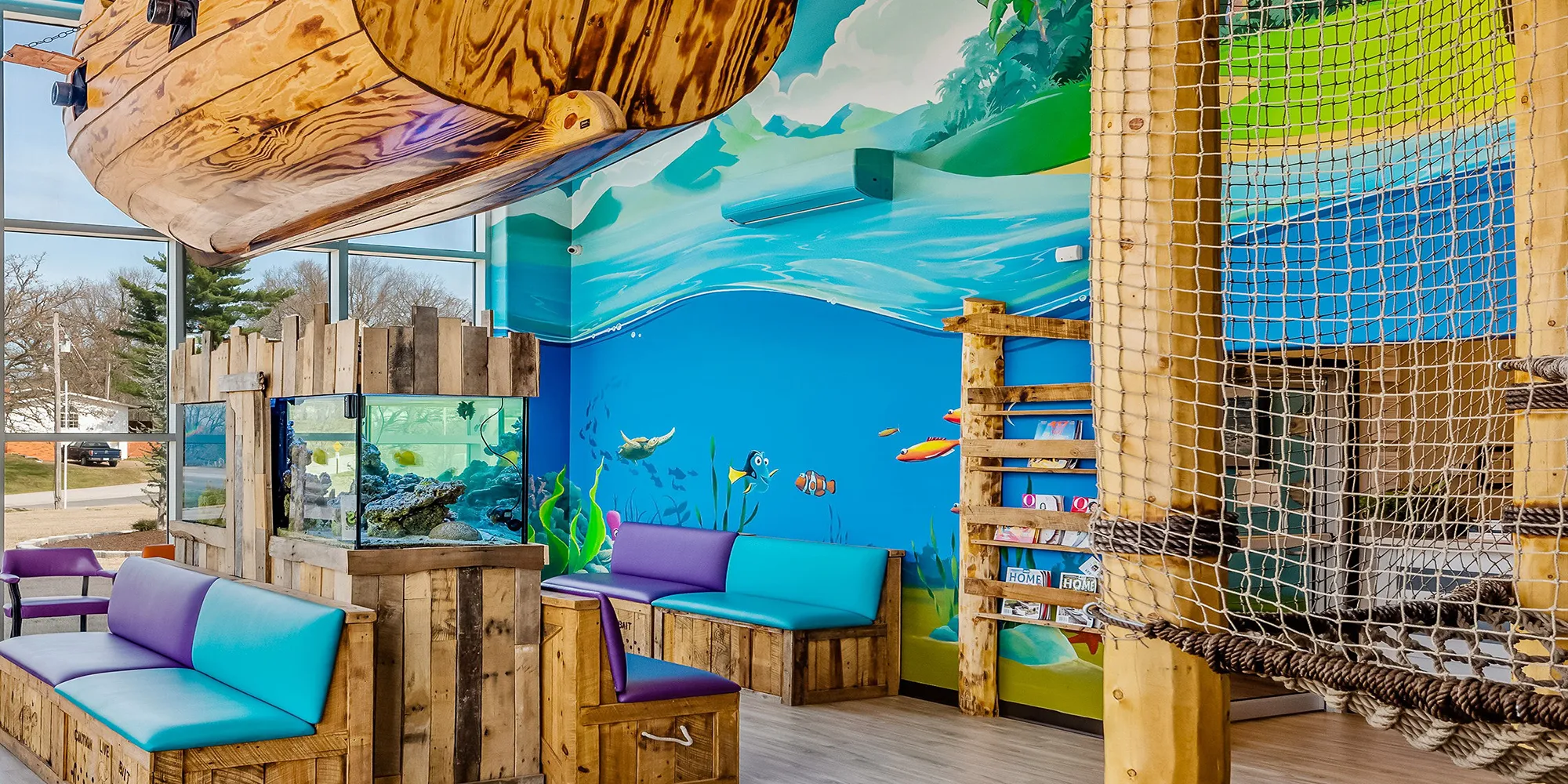 The Super Smiles lobby, rope-net climbing apparatus, fish tank, pirate-ship hideout, and aquatic banquette seating in one frame